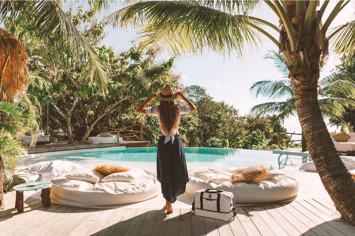 women overlooking  pool on vacation with weekender bag