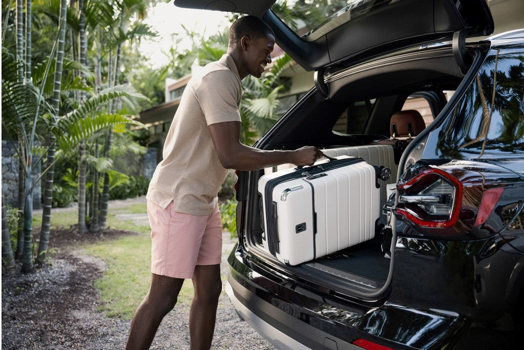 Man putting a Travelpro X Travel + Leisure carry on suitcase inside the trunk of a car.